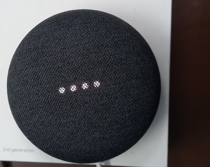 Google Nest Mini speaker in listening mode with four white lights blinking.