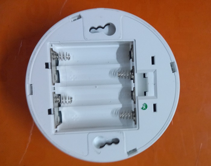 Obverse side of a wireless smoke detector with battery compartment visible. 